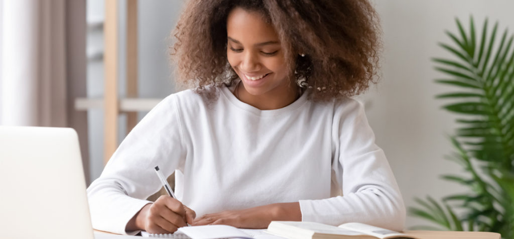 Adolescente assise Ă un bureau Ă la maison avec un ordinateur portable et des livres ouverts.